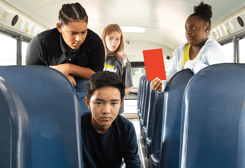 A student is being bullied on a school bus and another girl is pulling a Red Card to stop the bullying.